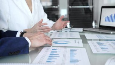 Ekonomi uzmanları finansal verileri analiz ediyor, pazar eğilimlerini tartışıyor ve bir dizüstü bilgisayar ekranındaki çizelge ve grafiklerle raporları gözden geçiriyor ve şirket planlama toplantısında basılı belgeler hazırlıyorlar.