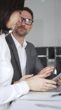 Takım elbiseli ve gözlüklü bir iş adamı önemli bir ofis toplantısında bayan bir meslektaşını dikkatle dinliyor, tartışma ve problem çözme üzerine yoğunlaşıyor, kurumsal strateji planlıyor.