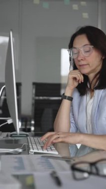 Uzun saatler süren veri girişi sırasında dijital yorgunluk ve göz yorgunluğu yaşayan ve ofis masasındaki bilgisayar klavyesine yazı yazan gözlüklü kadın, stres ve tükenmişliği yansıtıyor.