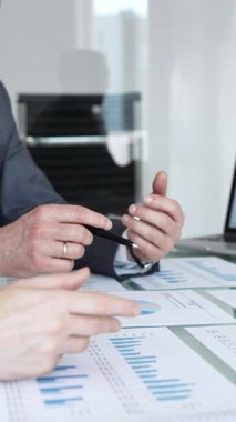 İş adamları, grafikleri ve kağıt dökümanlarını grafiklerle gösteren tabletle yakın etkileşim halinde, mali analiz, veri değerlendirmesi ve stratejik planlamaya odaklı olarak ellerini uzatıyorlar.