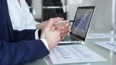 İş dünyası ekibi finansal verileri ve pazar eğilimlerini analiz ediyor, satış performansı, yatırım büyümesi ve stratejisini bir dizüstü bilgisayar ekranında çizelgeler ve kağıtlarla yapılan bir şirket toplantısında tartışıyor.