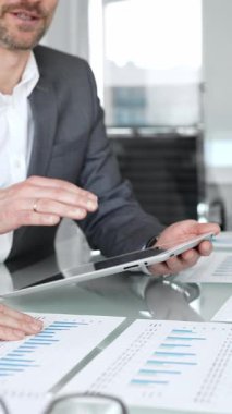 İş adamları, grafikleri ve kağıt dökümanlarını grafiklerle gösteren tabletle yakın etkileşim halinde, mali analiz, veri değerlendirmesi ve stratejik planlamaya odaklı olarak ellerini uzatıyorlar.