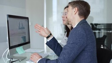 Bilgisayarda birlikte çalışan iki iş arkadaşı ekranda gösterilen grafik ve grafiklere işaret ederek veri analizini tartışıyor. İş insanları kavramı