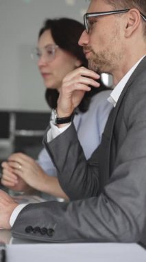 Resmi giyinmiş iki iş adamı, modern ofis ortamında yapılan bir toplantıda, bilgileri analiz ediyor ve bir proje üzerinde işbirliği yapıyorlar.