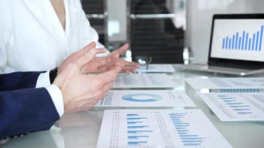Ekonomi uzmanları finansal verileri analiz ediyor, pazar eğilimlerini tartışıyor ve bir dizüstü bilgisayar ekranındaki çizelge ve grafiklerle raporları gözden geçiriyor ve şirket planlama toplantısında basılı belgeler hazırlıyorlar.
