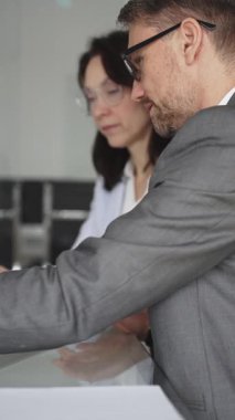 Resmi giyinmiş iki iş adamı, modern ofis ortamında yapılan bir toplantıda, bilgileri analiz ediyor ve bir proje üzerinde işbirliği yapıyorlar.