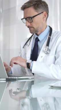 Beyaz önlük ve steteskop giyen doktor dizüstü bilgisayarda çalışıyor, teletıp danışmanlığı yapıyor ya da tıbbi rapor yazıyor. İlaç ve sağlık hizmetleri