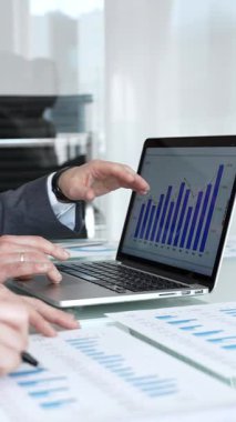 Modern bir ofis masasında iş birliği yapan iş adamları. Dizüstü bilgisayardaki mali tabloları ve basılı raporları analiz ediyorum. Stratejik iş kararları almak için verileri tartışmak ve notlar almak