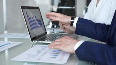 İş dünyası ekibi finansal verileri ve pazar eğilimlerini analiz ediyor, satış performansı, yatırım büyümesi ve stratejisini bir dizüstü bilgisayar ekranında çizelgeler ve kağıtlarla yapılan bir şirket toplantısında tartışıyor.