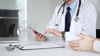 Doktorun hastaya danışması, bir klinik masasında tablet kullanması modern tıp ve dijital sağlık hizmetleri teşhisini sembolize ediyor. Tıp, sağlık ve bilim konsepti