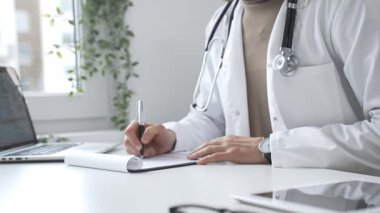 Laboratuvar önlüğü ve steteskop giyen doktor tıbbi reçete yazıyor ya da ofis masasında oturan tıbbi belgeleri dolduruyor. İlaç ve sağlık hizmetleri