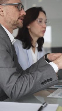Takım elbiseli ve gözlüklü bir iş adamı önemli bir ofis toplantısında bayan bir meslektaşını dikkatle dinliyor, tartışma ve problem çözme üzerine yoğunlaşıyor, kurumsal strateji planlıyor.
