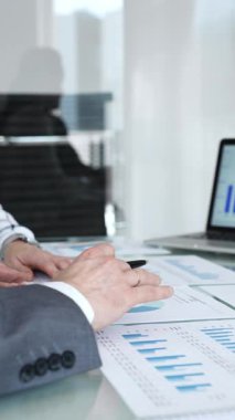 Pazar büyümesi ve mali performansı tartışan iş adamları, bir ofis toplantısı sırasında basılı raporları incelerken bir bar tablosunu gösteren bir dizüstü bilgisayara işaret ediyorlar