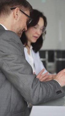 Resmi giyinmiş iki iş adamı, modern ofis ortamında yapılan bir toplantıda, bilgileri analiz ediyor ve bir proje üzerinde işbirliği yapıyorlar.