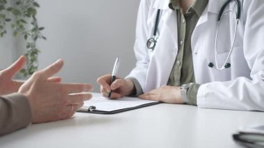 Doktor kadın, erkek hasta sağlığıyla ilgili endişeleri dinliyor ve parlak, modern bir klinikteki muayenede reçete yazıyor. Kapatın. İlaç ve sağlık hizmetleri kavramı.