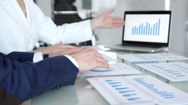 Ekonomi uzmanları finansal verileri analiz ediyor, pazar eğilimlerini tartışıyor ve bir dizüstü bilgisayar ekranındaki çizelge ve grafiklerle raporları gözden geçiriyor ve şirket planlama toplantısında basılı belgeler hazırlıyorlar.