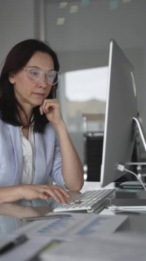 Uzun saatler süren veri girişi sırasında dijital yorgunluk ve göz yorgunluğu yaşayan ve ofis masasındaki bilgisayar klavyesine yazı yazan gözlüklü kadın, stres ve tükenmişliği yansıtıyor.