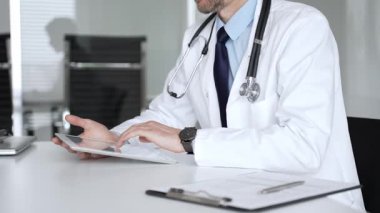 Beyaz önlüklü doktor ve steteskop modern dijital tablet üzerinde yazarak hastalara sağlık hizmeti ve sanal destek sağlıyor. Tıp, sağlık ve bilim konsepti