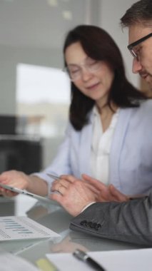 Resmi giyinmiş iki iş adamı, modern ofis ortamında yapılan bir toplantıda, bilgileri analiz ediyor ve bir proje üzerinde işbirliği yapıyorlar.