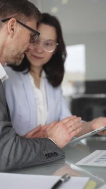 Resmi giyinmiş iki iş adamı, modern ofis ortamında yapılan bir toplantıda, bilgileri analiz ediyor ve bir proje üzerinde işbirliği yapıyorlar.