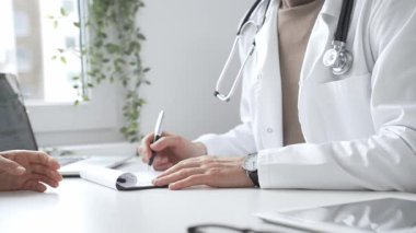 Doktor, parlak ve modern bir klinikteki muayene sırasında hasta sağlığıyla ilgili endişeleri dinliyor ve reçete yazıyor. İlaç ve sağlık hizmetleri kavramı.