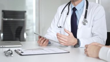 Doktorun hastaya danışması, bir klinik masasında tablet kullanması modern tıp ve dijital sağlık hizmetleri teşhisini sembolize ediyor. Tıp, sağlık ve bilim konsepti