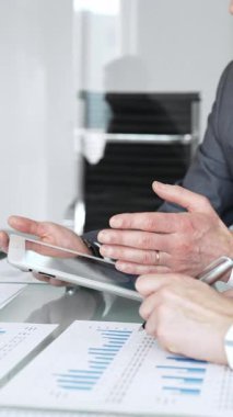 İş adamları, grafikleri ve kağıt dökümanlarını grafiklerle gösteren tabletle yakın etkileşim halinde, mali analiz, veri değerlendirmesi ve stratejik planlamaya odaklı olarak ellerini uzatıyorlar.