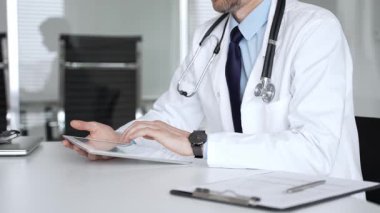 Beyaz önlüklü doktor ve steteskop modern dijital tablet üzerinde yazarak hastalara sağlık hizmeti ve sanal destek sağlıyor. Tıp, sağlık ve bilim konsepti