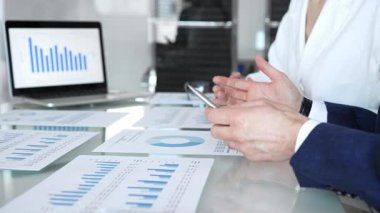 Ekonomi uzmanları finansal verileri analiz ediyor, pazar eğilimlerini tartışıyor ve bir dizüstü bilgisayar ekranındaki çizelge ve grafiklerle raporları gözden geçiriyor ve şirket planlama toplantısında basılı belgeler hazırlıyorlar.