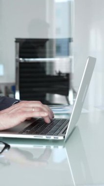 İşadamı işine yoğunlaşır, dizüstü bilgisayarda yazar, iş stratejilerini ve çözümleri düşünceli bir şekilde değerlendirirken, modern ofis ortamında profesyonel görevleri yönetir.