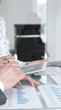 İş adamları, grafikleri ve kağıt dökümanlarını grafiklerle gösteren tabletle yakın etkileşim halinde, mali analiz, veri değerlendirmesi ve stratejik planlamaya odaklı olarak ellerini uzatıyorlar.