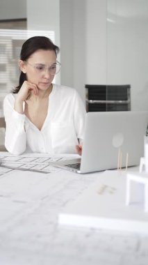 Kadın mimar, hassas ve profesyonel odaklı yenilikçi bir konut tasarımını ölçmek ve arıtmak için araçlar kullanarak, masa başında çağdaş yapı modeli ve planlarını inceler.