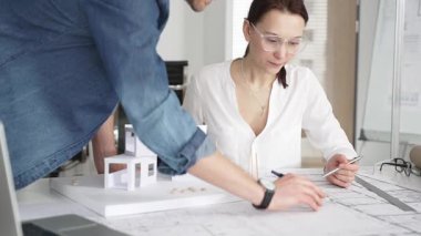 Mimarlar yeni bir bina projesi geliştiriyorlar. Meslektaşları mimari bir model, sergilenen tasarım, planlama ve takım çalışması üzerinde cetvelle çalışan bir kadın profesyonel çizim.