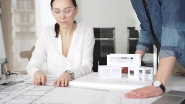 Mimarlar yeni bir bina projesi geliştiriyorlar. Meslektaşları mimari bir model, sergilenen tasarım, planlama ve takım çalışması üzerinde cetvelle çalışan bir kadın profesyonel çizim.