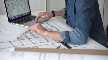 Profesyonel mimar, mimari planlarla kaplı bir masanın üzerine ayrıntılı planlar çiziyor. Hem geleneksel araçlardan hem de modern dizüstü bilgisayarlardan tasarım için yararlanmak. Planlama. Ve kentsel gelişim