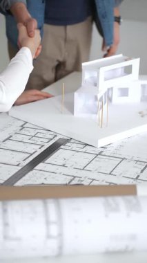 Mimarlar, tasarım ayrıntıları üzerinde işbirliği yaparak ve inşaat için yeni bir konut inşaatı projesi planlayarak, temiz bir masadaki planları ve ölçekli bir modeli inceleyecekler.