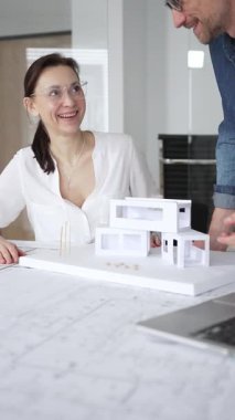 Mimarlar yeni bir bina projesi geliştiriyorlar. Meslektaşları mimari bir model, sergilenen tasarım, planlama ve takım çalışması üzerinde cetvelle çalışan bir kadın profesyonel çizim.