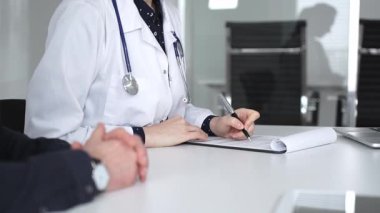 Beyaz önlüklü doktor, bir hastayla tıbbi istişare sırasında panoya notlar yazarak sağlık ve tedaviyi tartışıyor. Tıp, sağlık ve bilim konsepti