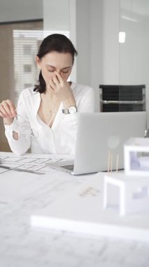 Kadın mimar, hassas ve profesyonel odaklı yenilikçi bir konut tasarımını ölçmek ve arıtmak için araçlar kullanarak, masa başında çağdaş yapı modeli ve planlarını inceler.