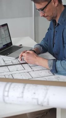 Profesyonel mimar, mimari planlarla kaplı bir masanın üzerine ayrıntılı planlar çiziyor. Hem geleneksel araçlardan hem de modern dizüstü bilgisayarlardan tasarım için yararlanmak. Planlama. Ve kentsel gelişim