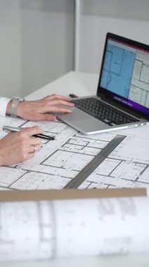 Kadın mimar, ayrıntılı bina planları üzerinde titizlikle çalışıyor. Masasına yayılmış. Mimari tasarımları parlak bir şekilde geliştirirken bir kalem ve cetvel kullanmak. Çağdaş ofis ortamı