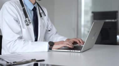 Teletıp, dijital kayıtlar ve hasta danışma işleri için dizüstü bilgisayarında steteskopla yazı yazan beyaz önlüklü bir doktor. Tıp, sağlık ve bilim konsepti
