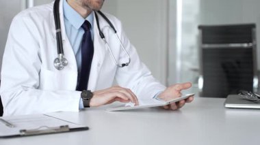 Beyaz önlüklü doktor ve steteskop modern dijital tablet üzerinde yazarak hastalara sağlık hizmeti ve sanal destek sağlıyor. Tıp, sağlık ve bilim konsepti