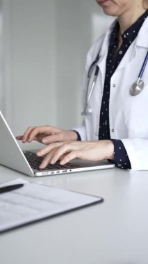 Beyaz önlüklü ve steteskoplu bir doktor dizüstü bilgisayarda daktilo kullanıyor, online sağlık kayıtlarını ve dijital tıbbi gelişmeleri yönetiyor. Tıp, sağlık ve bilim konsepti