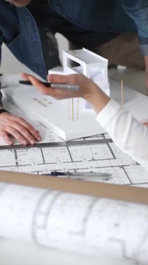 Mimarlar, tasarım ayrıntıları üzerinde işbirliği yaparak ve inşaat için yeni bir konut inşaatı projesi planlayarak, temiz bir masadaki planları ve ölçekli bir modeli inceleyecekler.