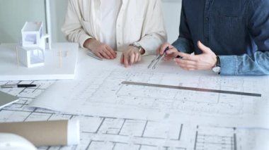 Mimarlar ve planlamacılar pusula ve dizüstü bilgisayarla ayrıntılı planları inceleyerek, bir konut projesinin kesin konut planlarını geliştirmek için bir ölçek modeli üzerinde işbirliği yapıyorlar