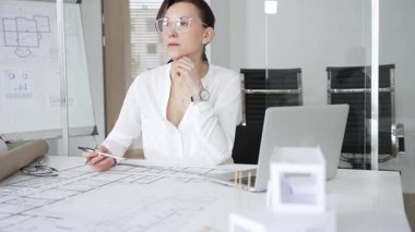 Kadın mimar, ayrıntılı bina planları üzerinde titizlikle çalışıyor. Masasına yayılmış. Mimari tasarımları parlak bir şekilde geliştirirken bir kalem ve cetvel kullanmak. Çağdaş ofis ortamı