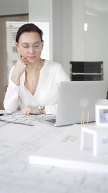 Kadın mimar, hassas ve profesyonel odaklı yenilikçi bir konut tasarımını ölçmek ve arıtmak için araçlar kullanarak, masa başında çağdaş yapı modeli ve planlarını inceler.