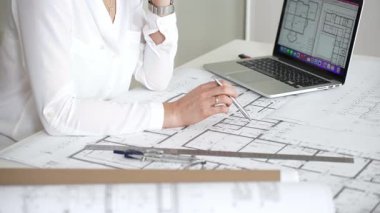 Ofiste bina planları üzerinde çalışan mimar, dizüstü bilgisayarla planlar ve kat planlarını analiz eden, yeni inşaat projeleri tasarlayan, konut ve ticari yapılar planlayan