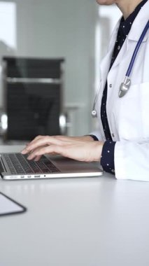 Beyaz önlüklü ve steteskoplu bir doktor dizüstü bilgisayarda daktilo kullanıyor, online sağlık kayıtlarını ve dijital tıbbi gelişmeleri yönetiyor. Tıp, sağlık ve bilim konsepti